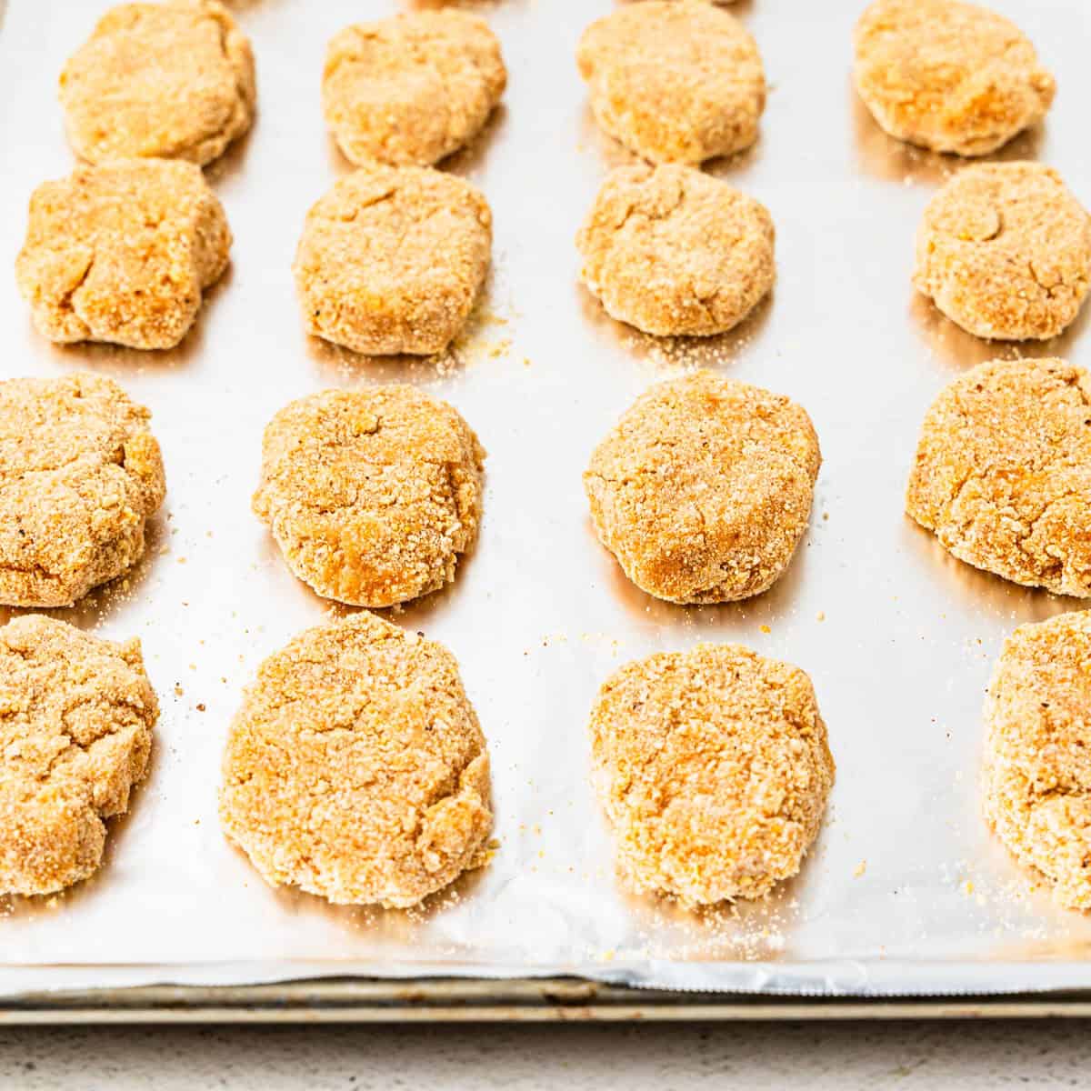 Uncooked chicken nuggets on a baking sheet.