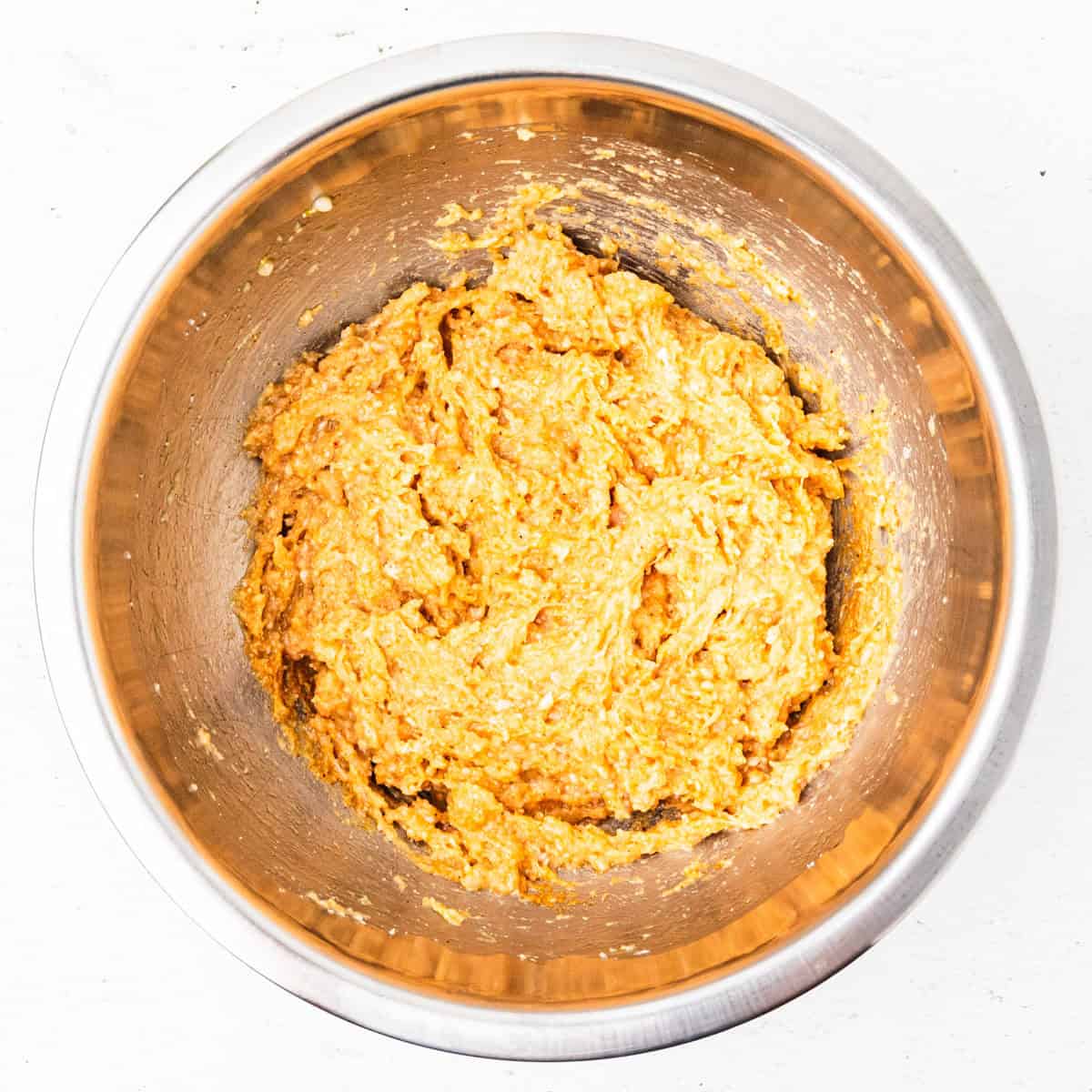 Ground chicken mixed with breadcrumbs and seasonings in a mixing bowl.
