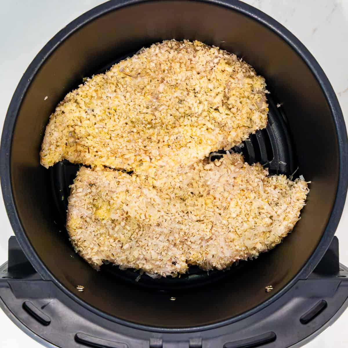 Breaded chicken in an air fryer basket before cooking.