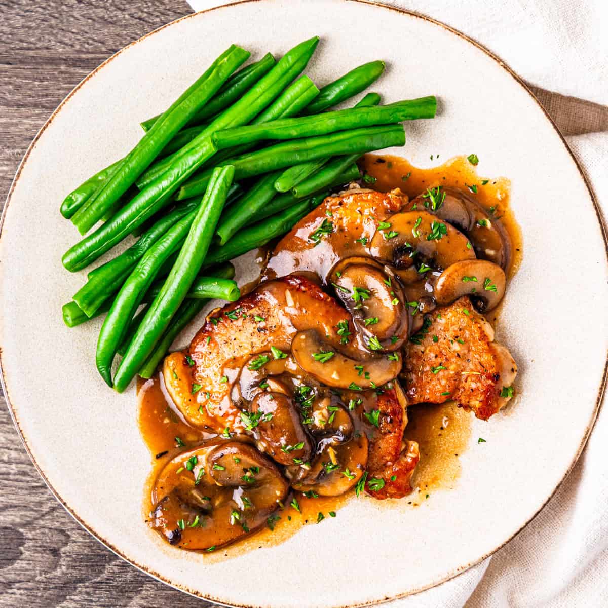 Pork chop marsala served on a plate with steamed green beans.