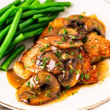 Pork chop marsala served on a plate with steamed green beans.
