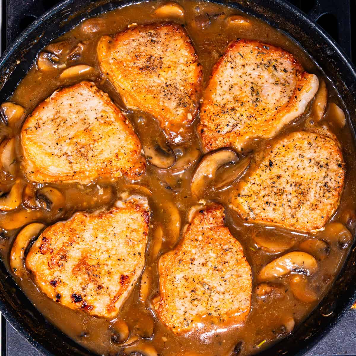 Pork chops with mushrooms and marsala sauce in a pan.