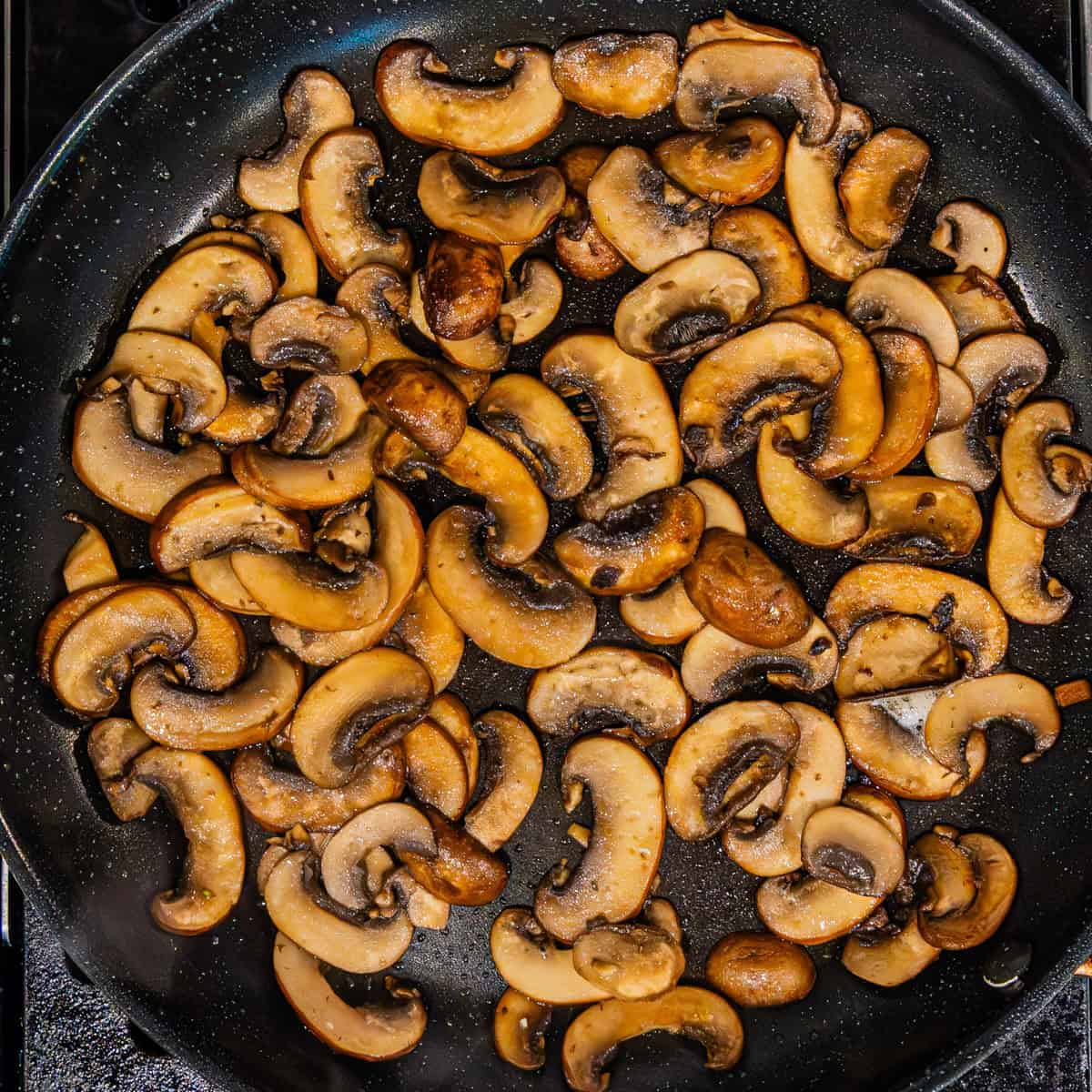 Sliced mushrooms cooking in a pan.