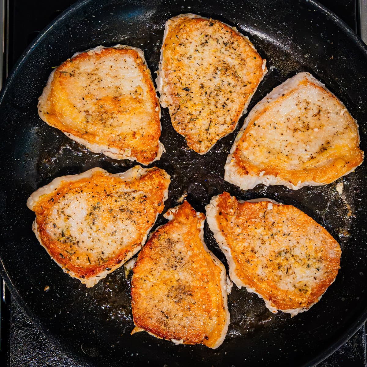 Pork chops being seared in a skillet.