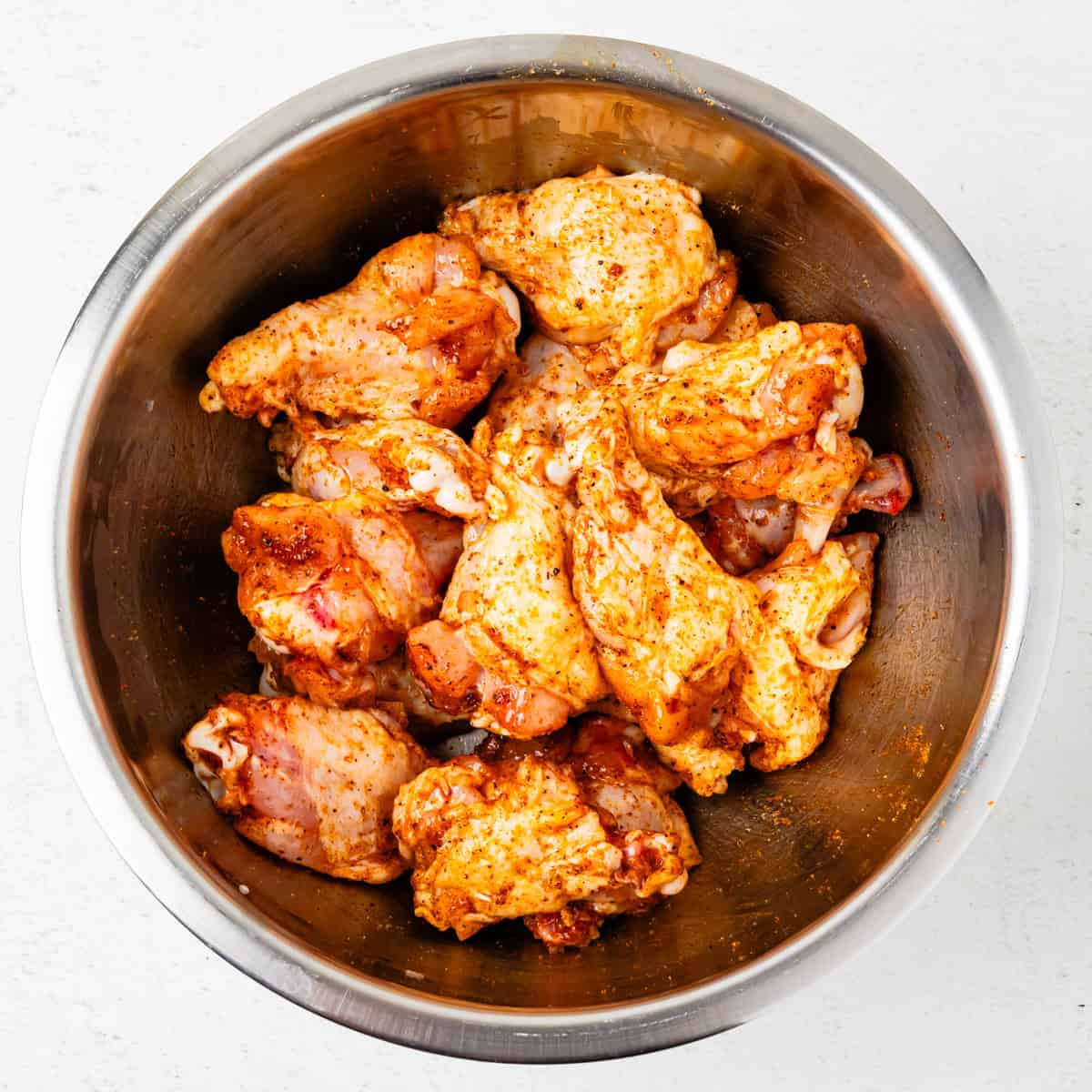 Chicken wings in a mixing bowl coated with barbecue rub.