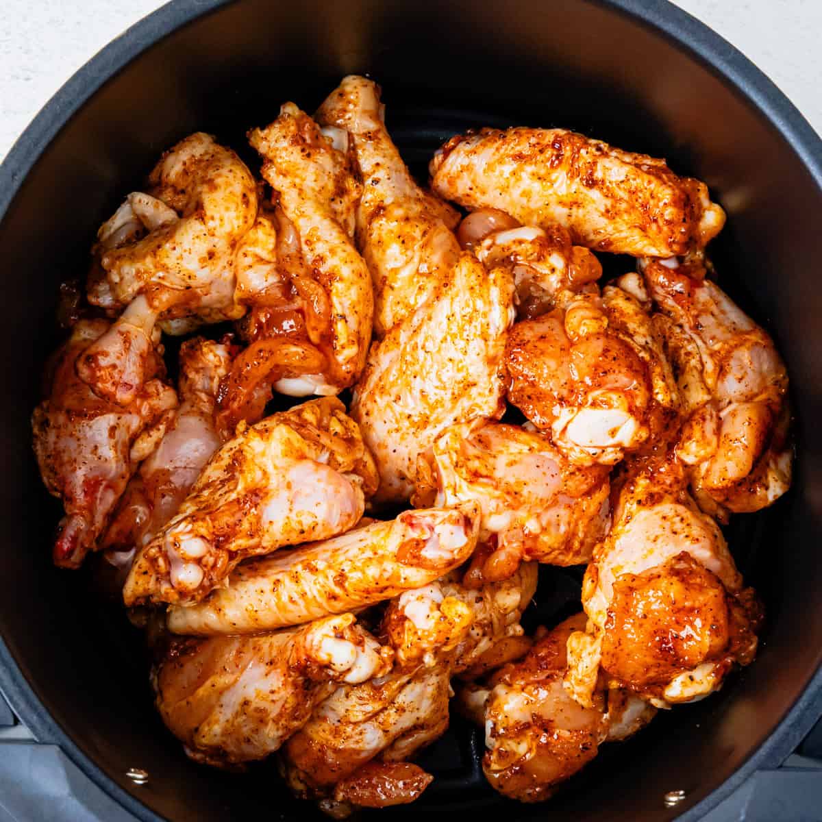 Chicken wings in an air fryer basket before cooking.