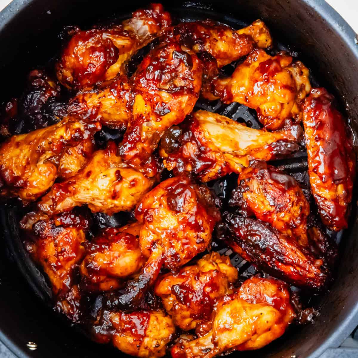 Cooked BBQ chicken wings in an air fryer basket.