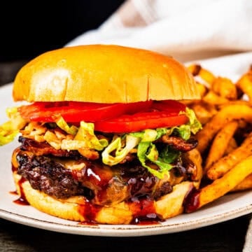 A bacon cheeseburger with barbecue sauce served on a plate with fries.