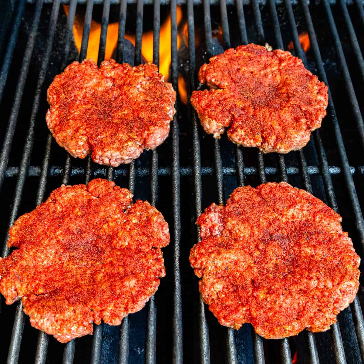 Seasoned hamburger patties cooking on a grill.
