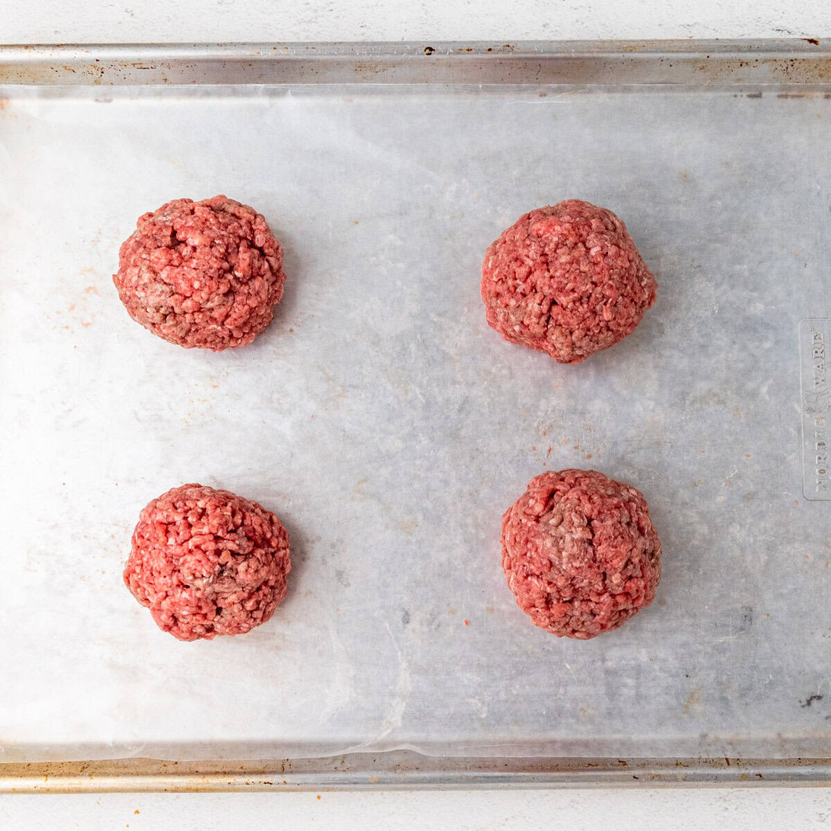 Balls of ground beef on a sheet pan.