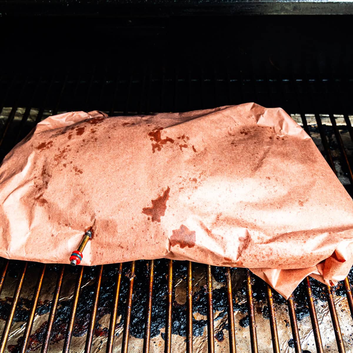 Brisket wrapped in butcher paper, cooking in a smoker.