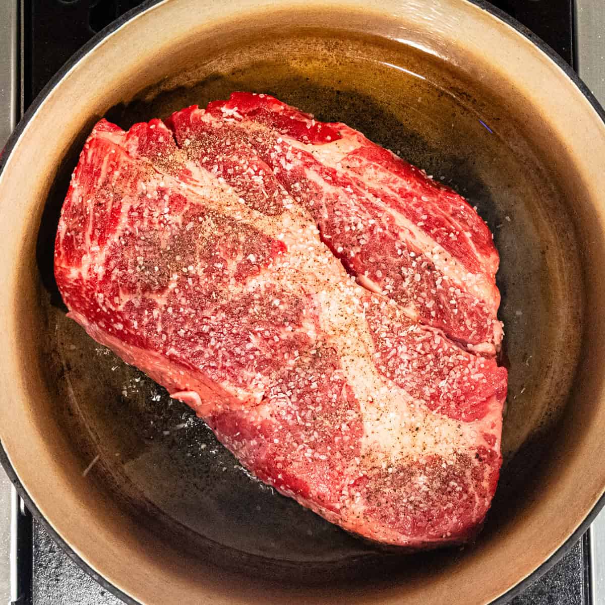 A seasoned chuck roast in a pot before being cooked.