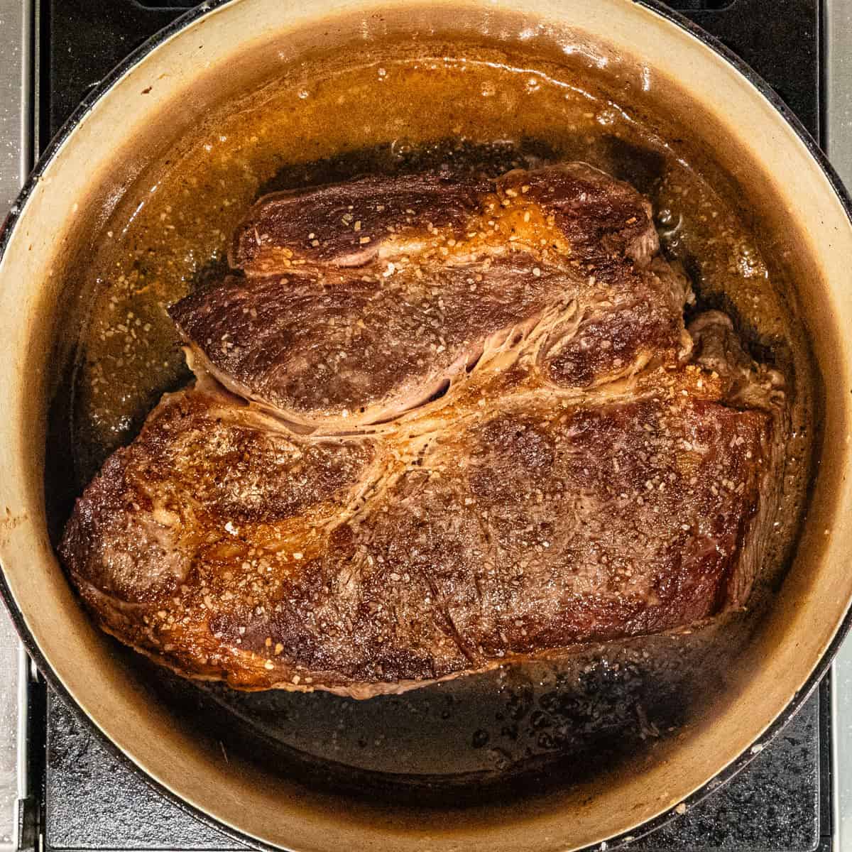 A bark brown seared chuck roast in pot.