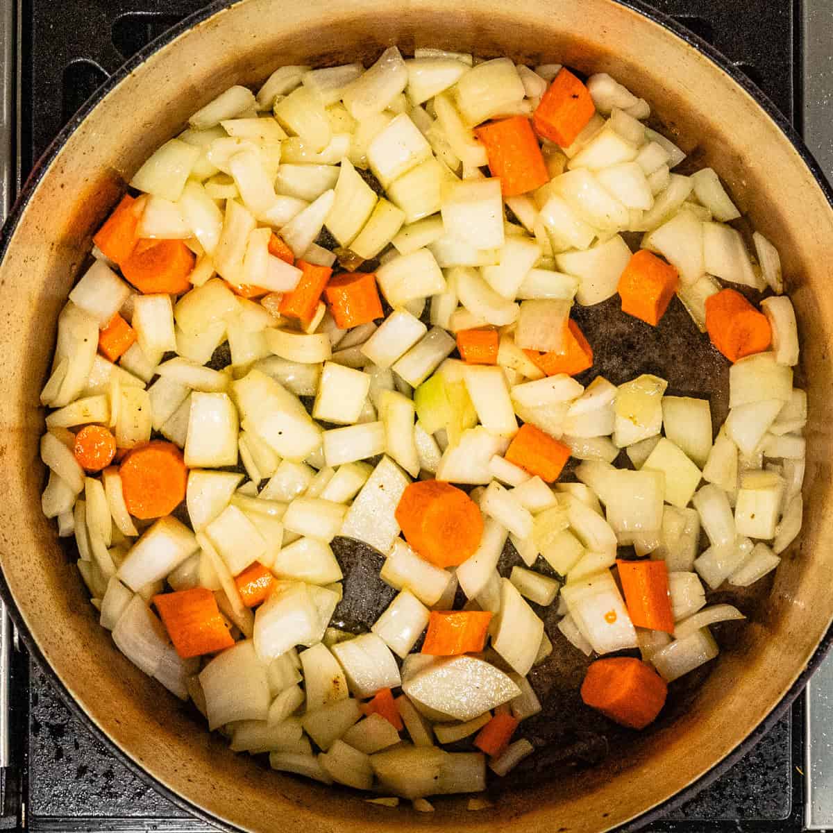 Chopped onions and carrots cooking in a pot.