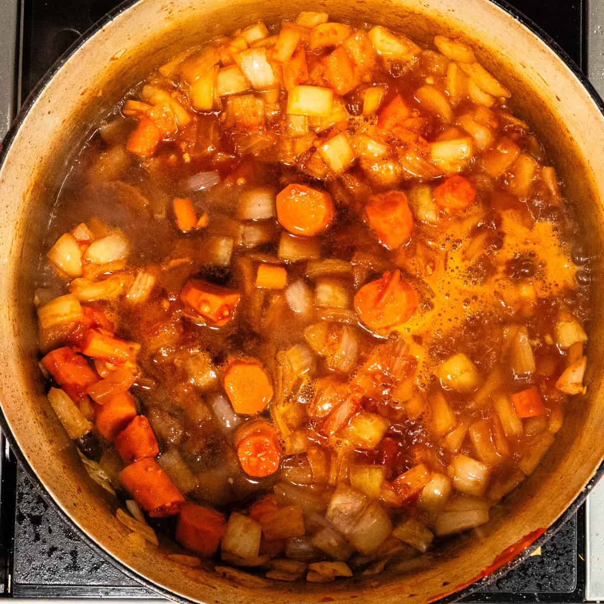 Braising liquids simmering in a pot with carrots and onions.