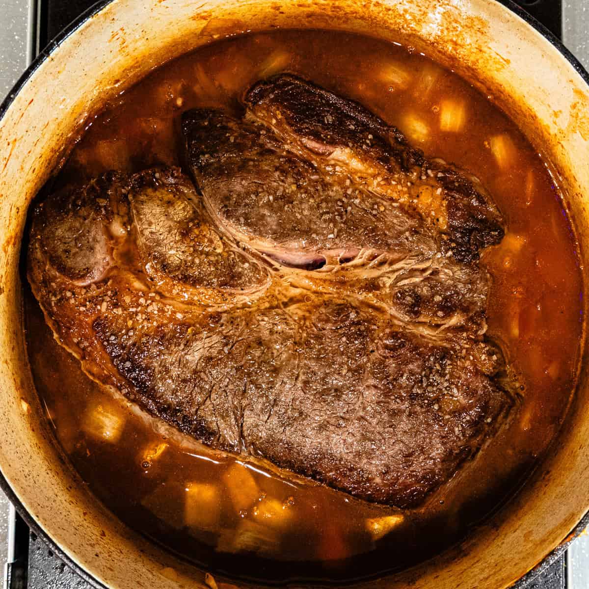 Chuck roast in a Dutch oven with braising liquids.