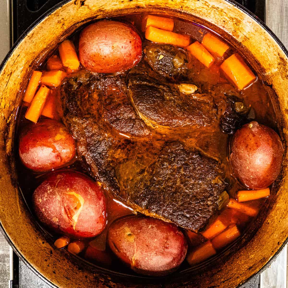 A finished braised chuck roast with potatoes and carrots in a Dutch oven.