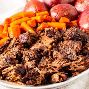 Braised chuck roast served on a platter with potatoes and carrots.