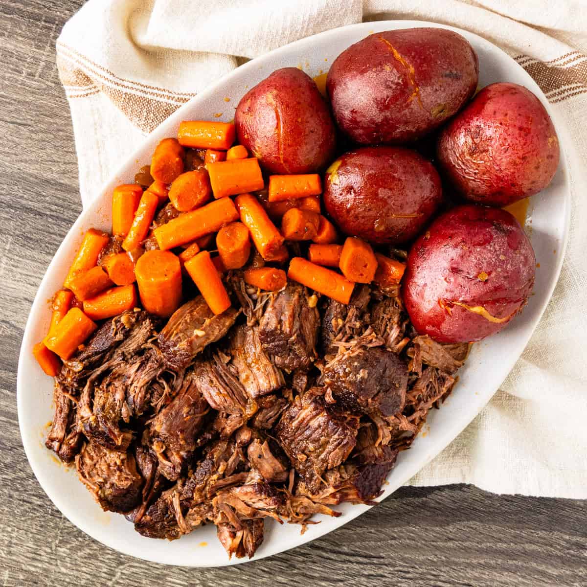 Shredded chunks of braised beef chuck on a platter with carrots and potatoes.