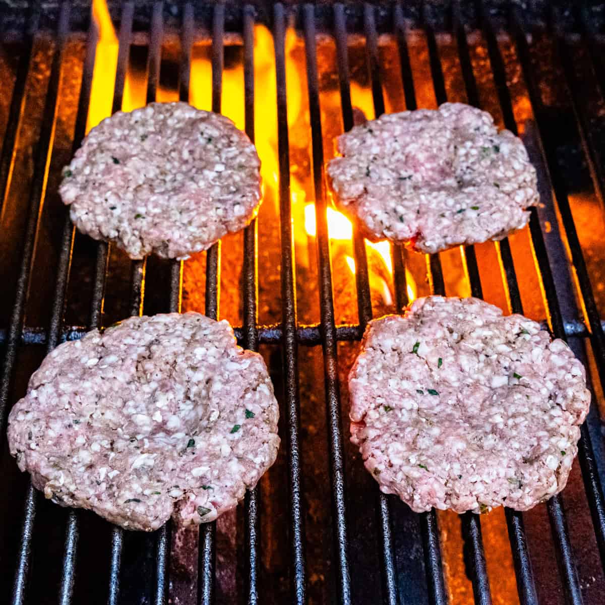 Lamb burger patties cooking on a flaming grill.