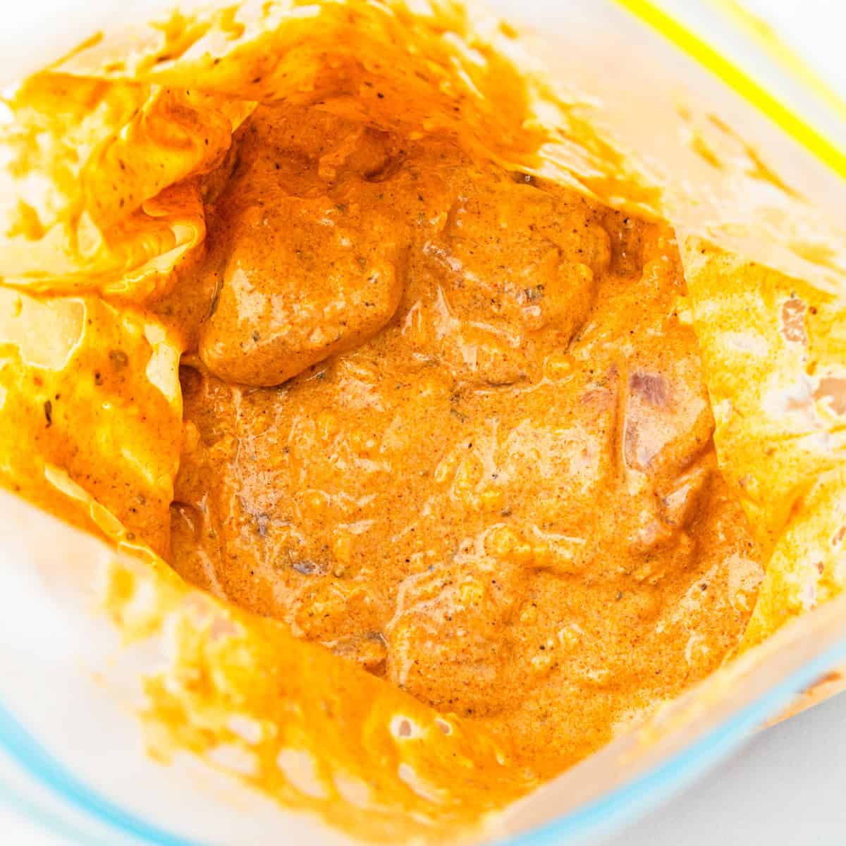 Chicken thighs mixed with marinade in a large plastic bag.