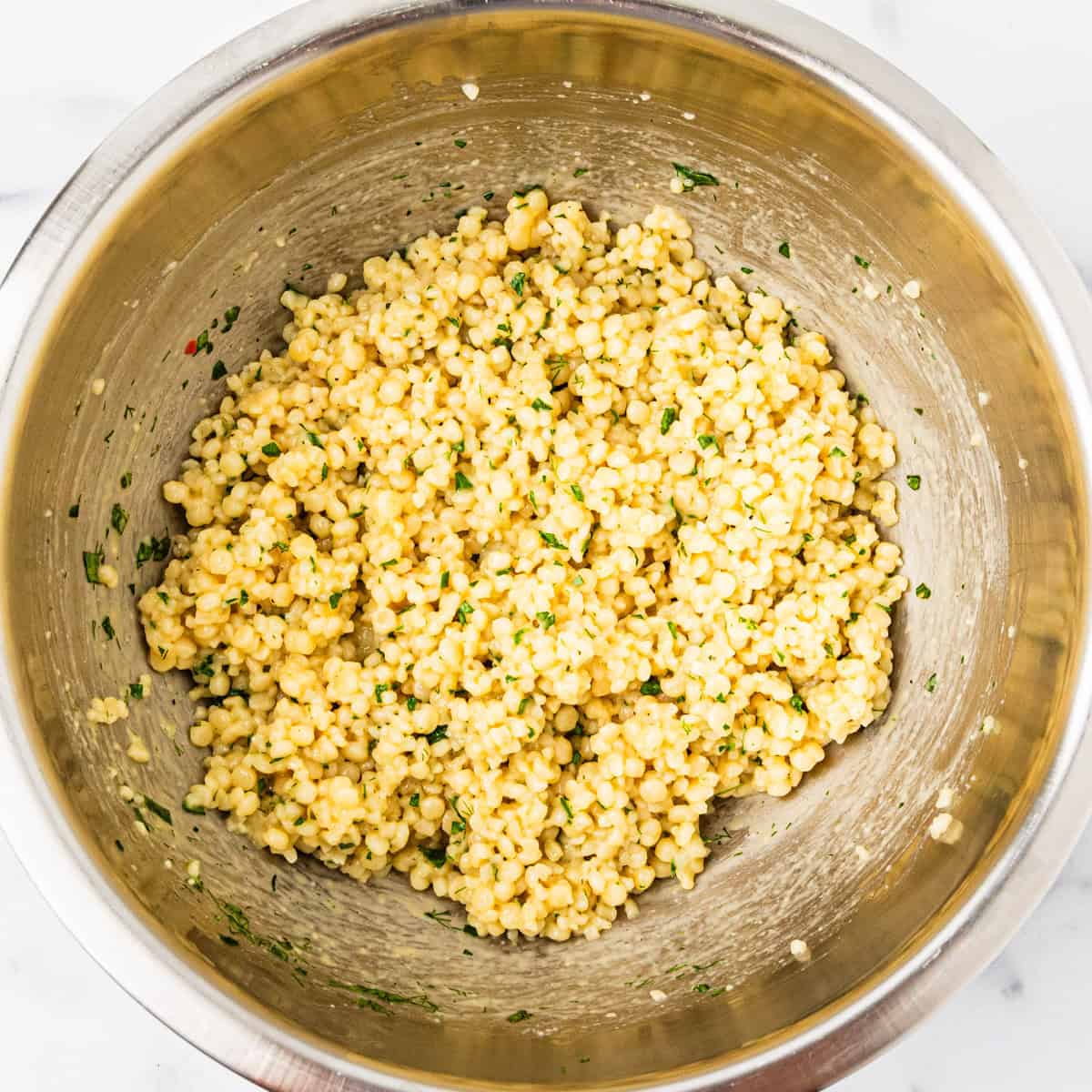 Couscous tossed with lemon and herb vinaigrette in a mixing bowl.