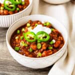 A bowl of turkey lentil chili topped with sour cream, green onions, and jalapeños.
