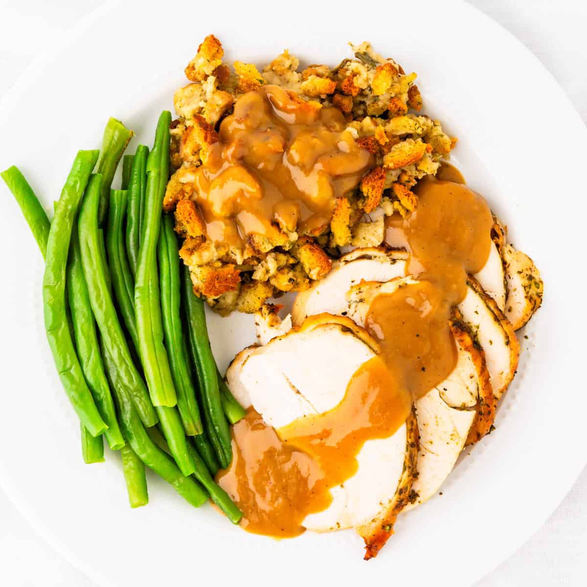 Roasted turkey breast and gravy on a plate with stuffing and green beans.